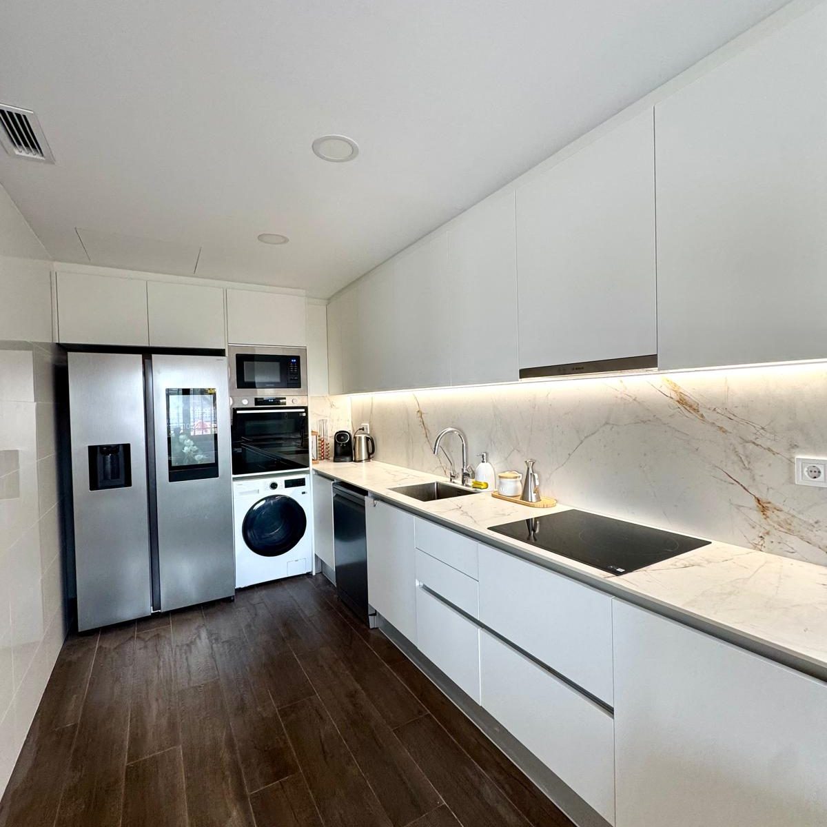 Cocina reformada en Castellbisbal con mobiliario blanco, encimera de mármol y suelo porcelánico imitación madera