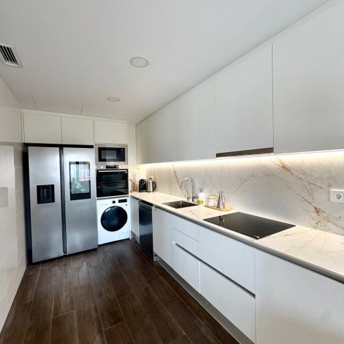 Cocina reformada en Castellbisbal con mobiliario blanco, encimera de mármol y suelo porcelánico imitación madera