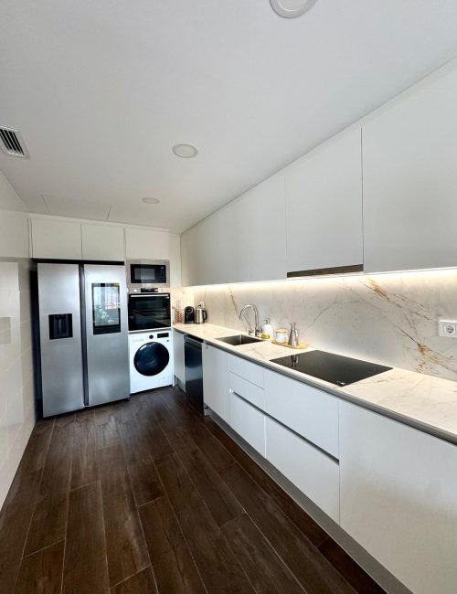 Cocina reformada en Castellbisbal con mobiliario blanco, encimera de mármol y suelo porcelánico imitación madera