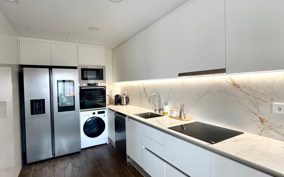 Cocina reformada en Castellbisbal con mobiliario blanco, encimera de mármol y suelo porcelánico imitación madera