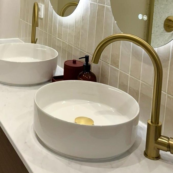 Baño con dos lavabos, dos espejos y grifos dorados